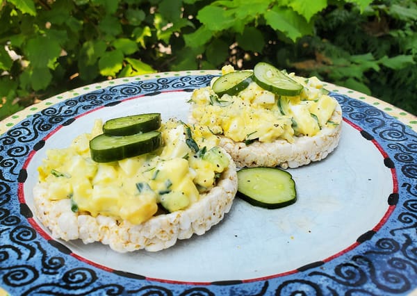 Egg salad on rice cakes, with quick pickles and fresh chives, displayed on a patterned blue plate.