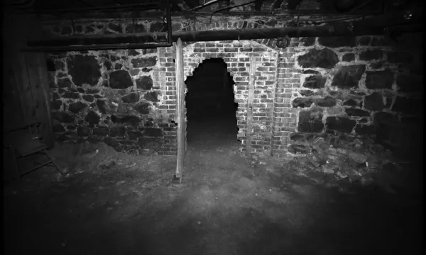 A black and white photo of a spooky, brick-lined underground tunnel.