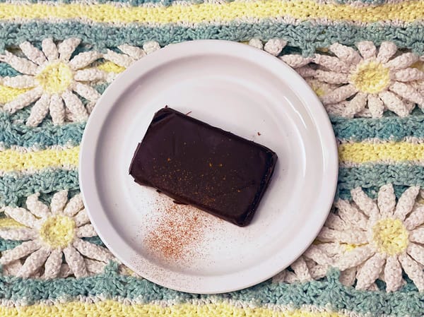 A homemade chocolate bar on a white plate, with a dusting of cinnamon, atop a flowery blanket.